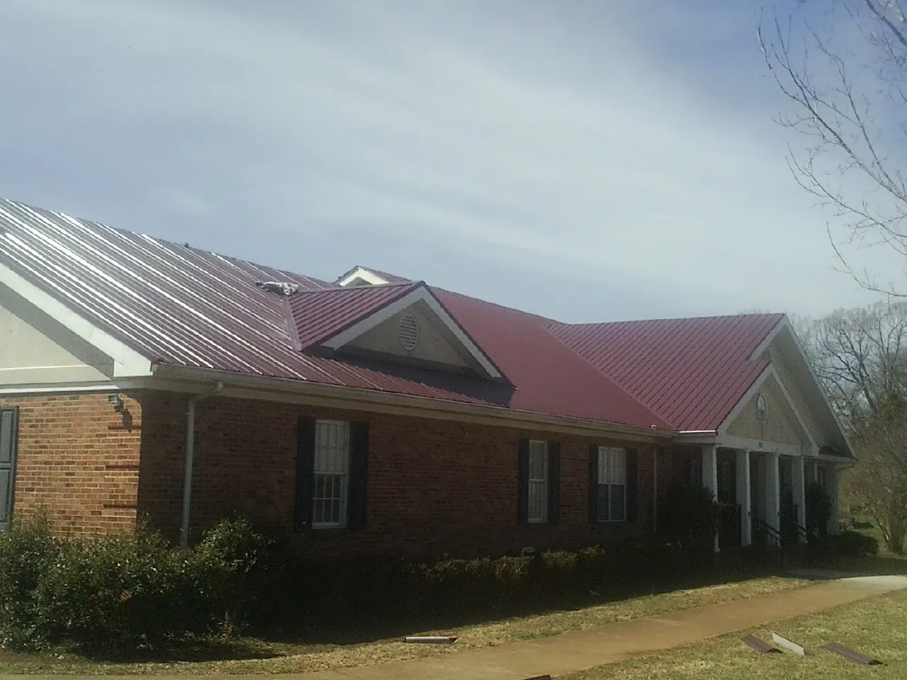 Red metal roof with gabled entries on a long brick building, from a Hail Damage Roof Repair job in Dorset
